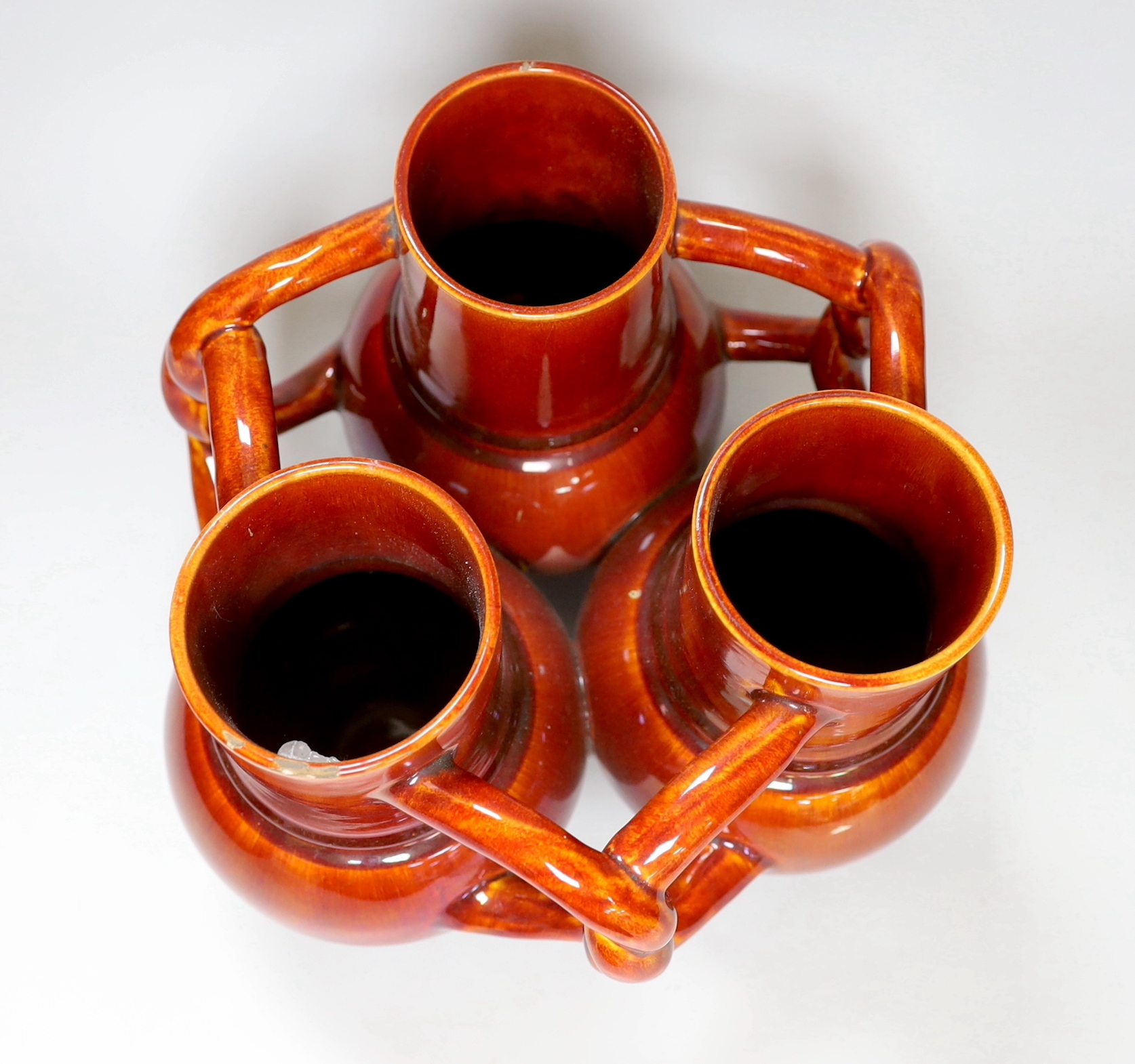 A Burmantofts Pottery three section fuddling cup with interwoven handles in dark burnt orange, stamped with marks to base, height 21cm